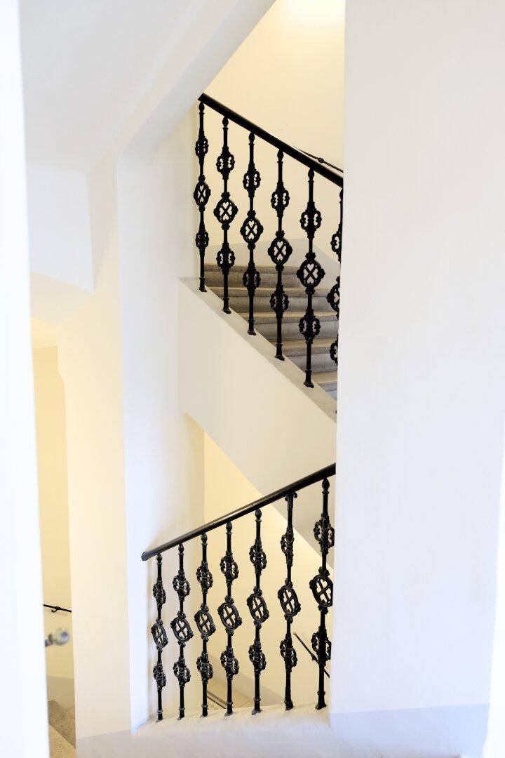 Elegantes Treppenhaus mit schmiedeeisernem Geländer und hellen Wänden in einem Altbau.