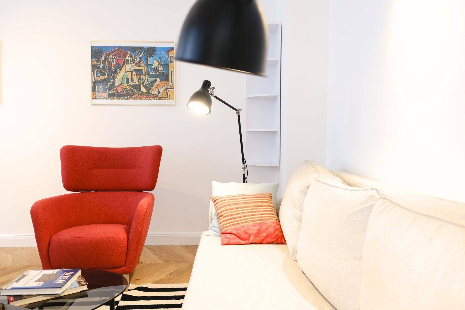 Gemütlicher Wohnbereich mit rotem Sessel, weißem Sofa und moderner Stehlampe auf Fischgrätparkett.