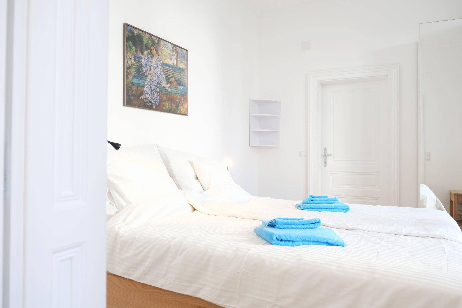 Schlafzimmer mit Doppelbett, weißer Bettwäsche und Kunstwerk an der Wand, vom Flur aus gesehen.