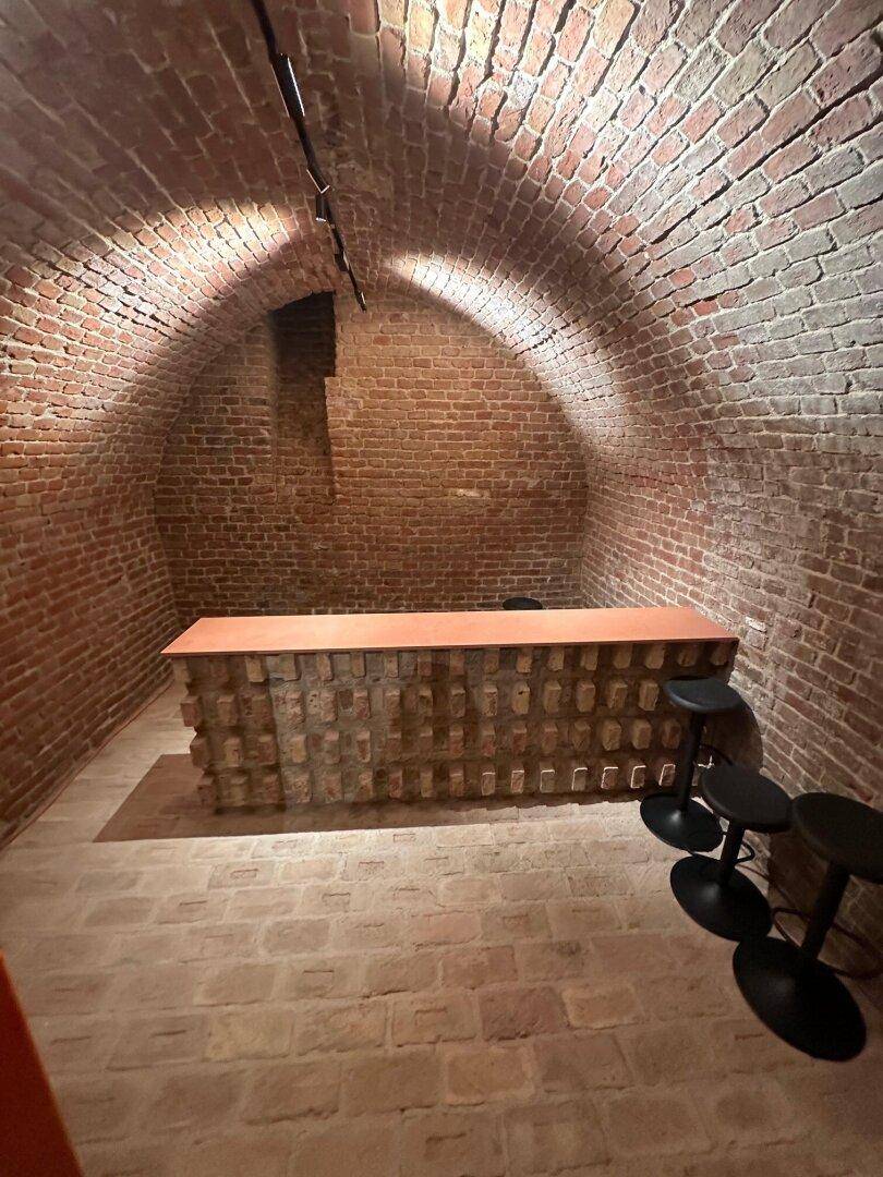 Rustikaler Kellerraum mit Ziegelgewölbe und einer modernen Bar mit Hockern.