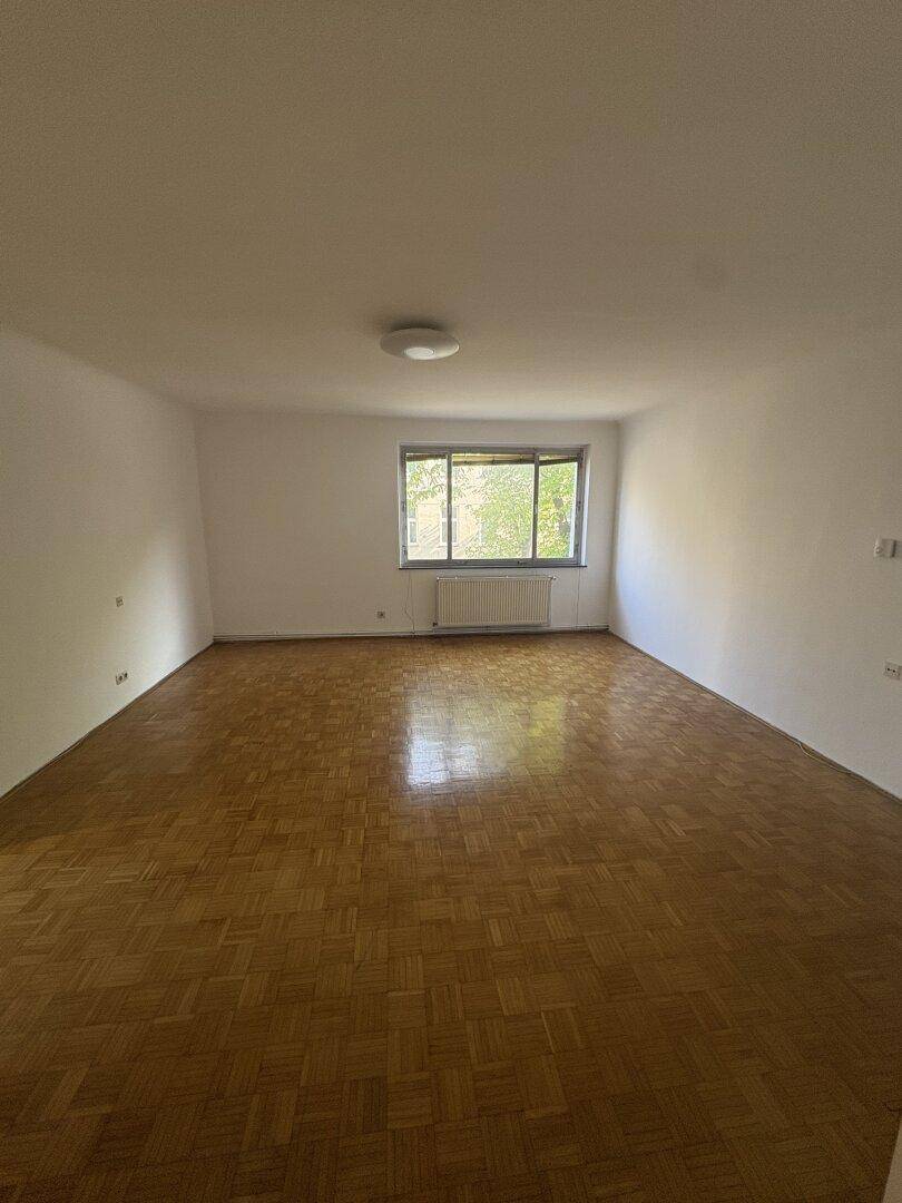 Heller Wohnbereich mit klassischem Parkettboden und einem Fenster mit Ausblick, ideal für entspannte Stunden.