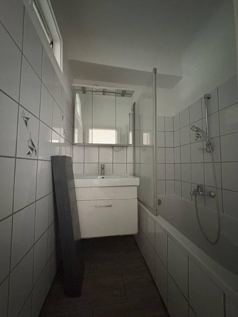 Modernes Badezimmer mit Badewanne, Waschbecken und Spiegelschrank, komplett mit weißen Fliesen ausgestattet.