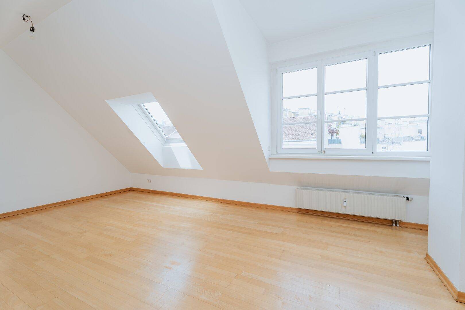 Geräumiges Dachgeschosszimmer mit Holzboden, Dachfenster und großen Fenstern für viel Tageslicht.