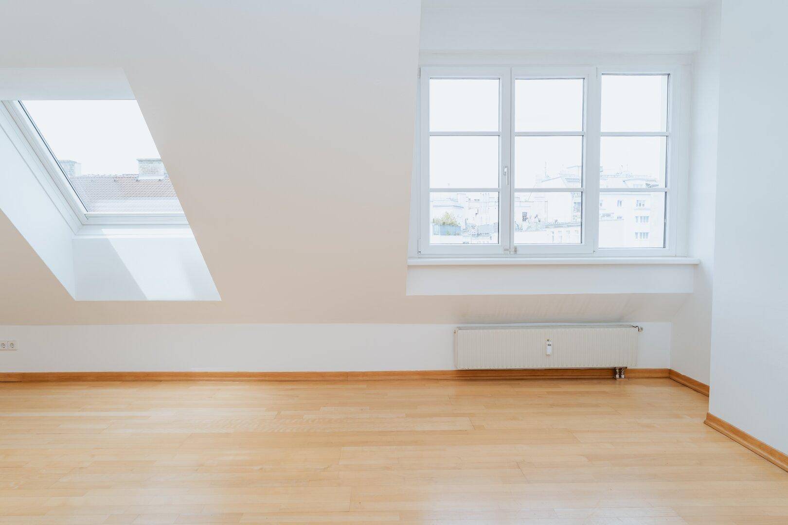Heller Wohnbereich im Dachgeschoss mit Holzboden, großem Fenster und Dachfenster.