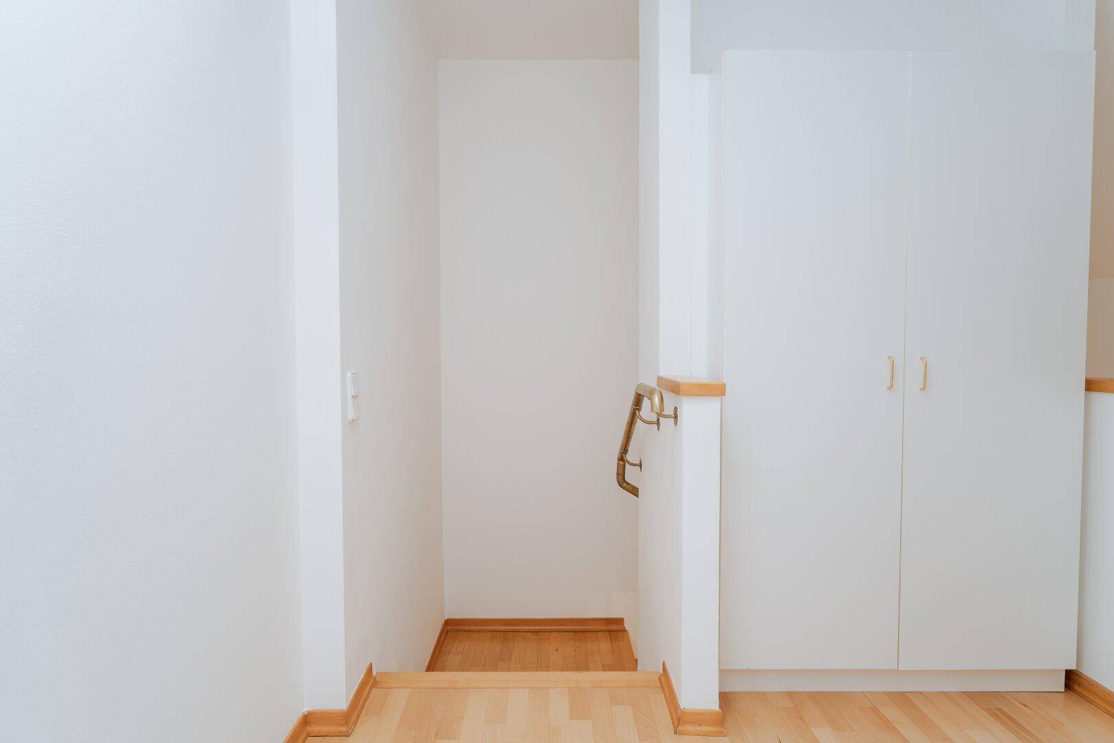 Heller Flurbereich mit Holzboden, Einbauschränken und Handlauf zur Treppe.