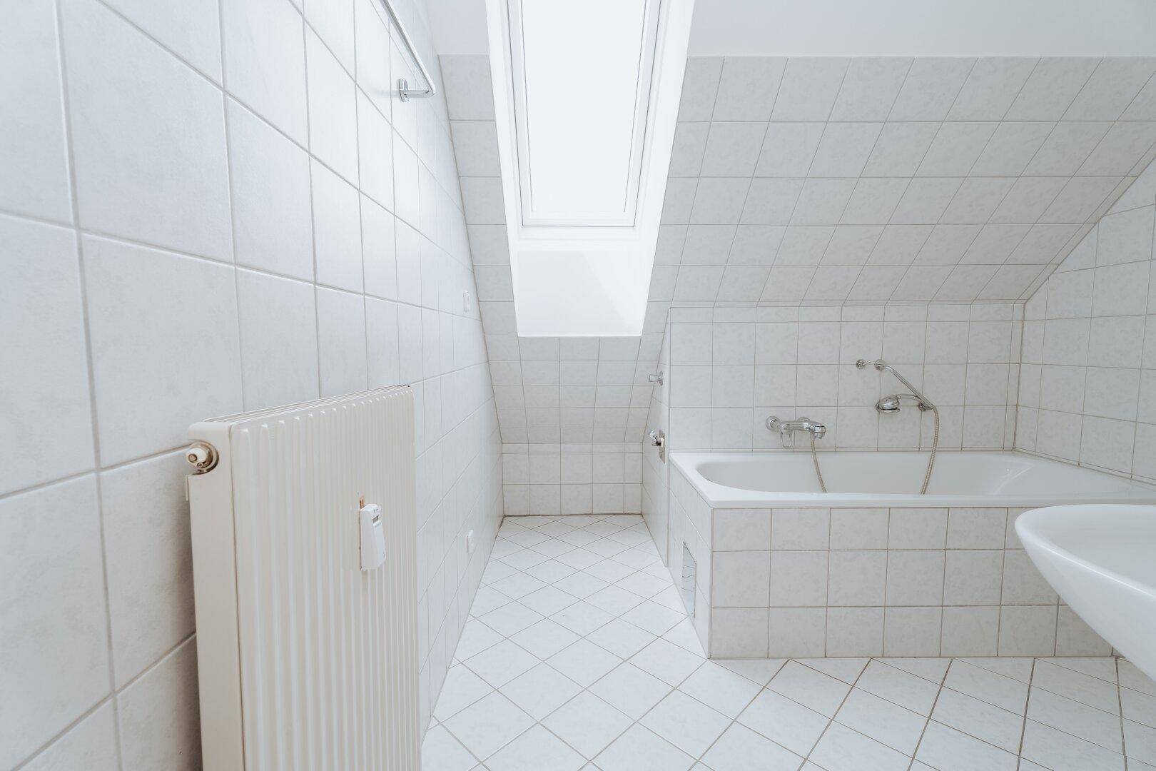 Helles Badezimmer mit weißen Fliesen, Badewanne und Dachfenster unter der Schräge.