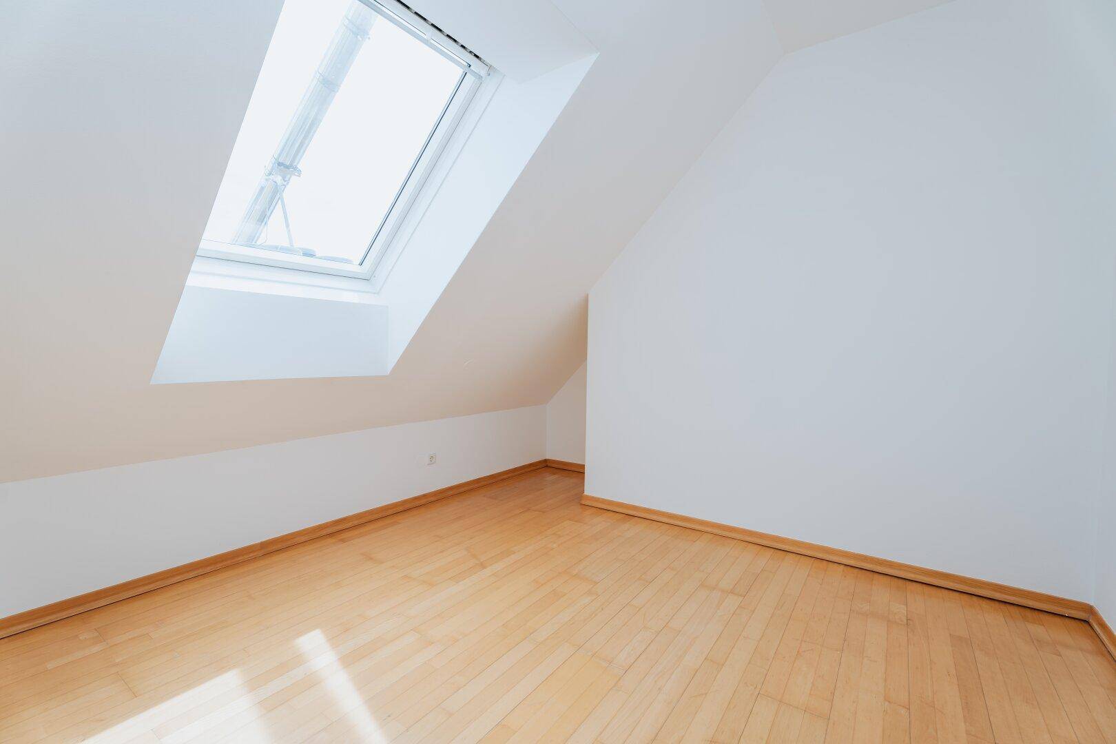 Gemütliches Schlafzimmer im Dachgeschoss mit Holzboden und viel Tageslicht durch das Dachfenster.