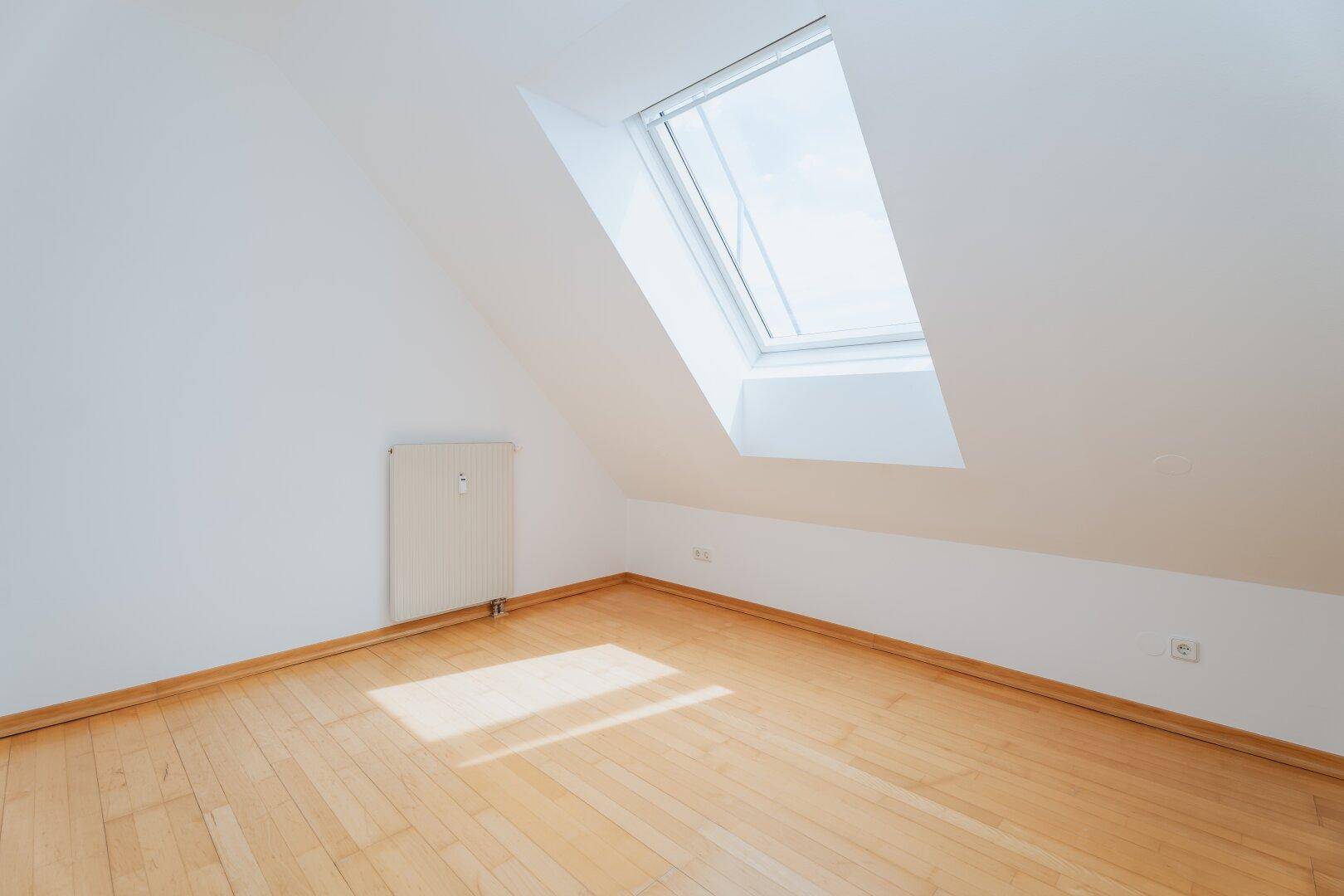 Helles Schlafzimmer im Dachgeschoss mit Holzboden und großem Dachfenster.