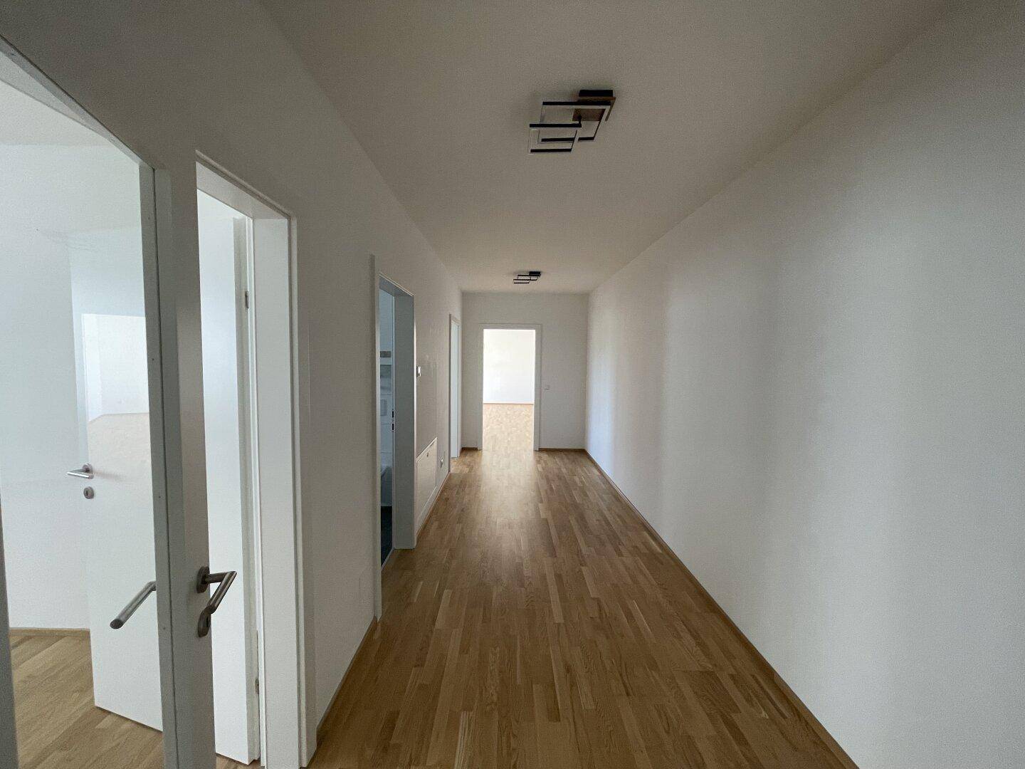 Langer, heller Flur mit Holzparkettboden und weißen Wänden, der zu weiteren Räumen führt.