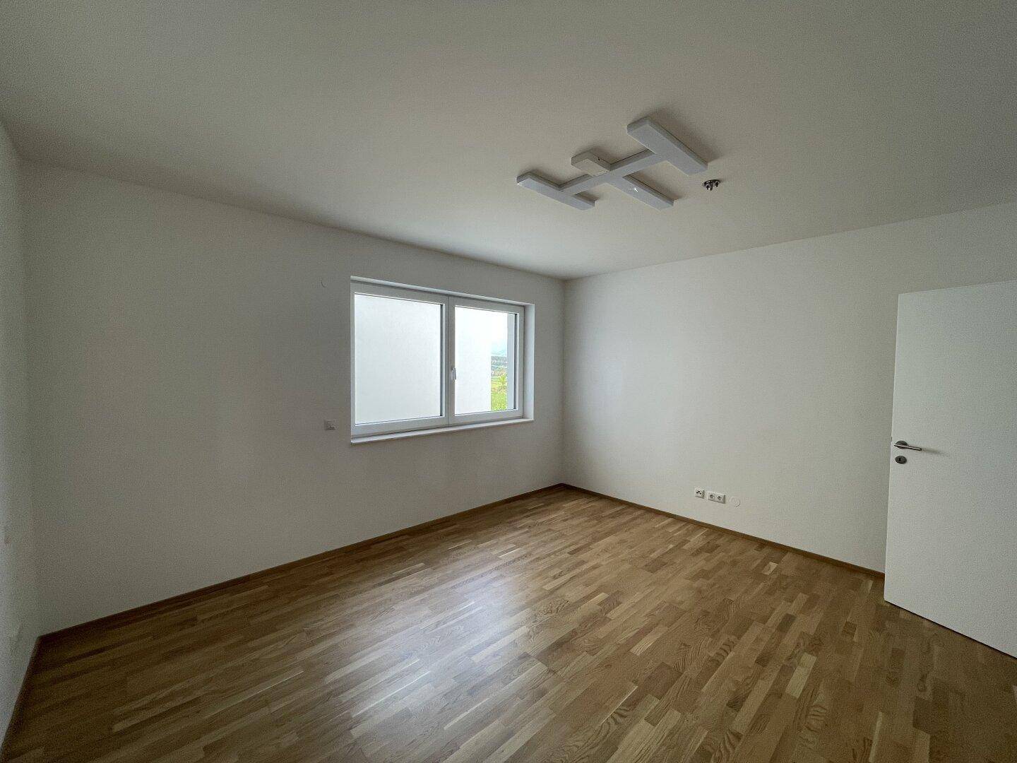 Helles Schlafzimmer mit Parkettboden und einem Fenster, bereit zur individuellen Gestaltung.