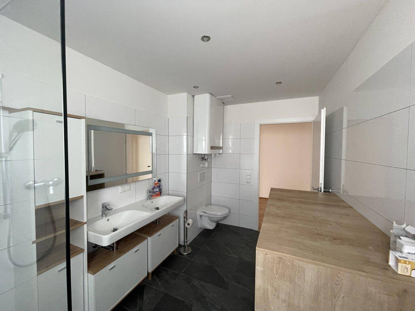 Geräumiges Badezimmer mit Doppelwaschbecken, wandhängendem WC und moderner Duschkabine.