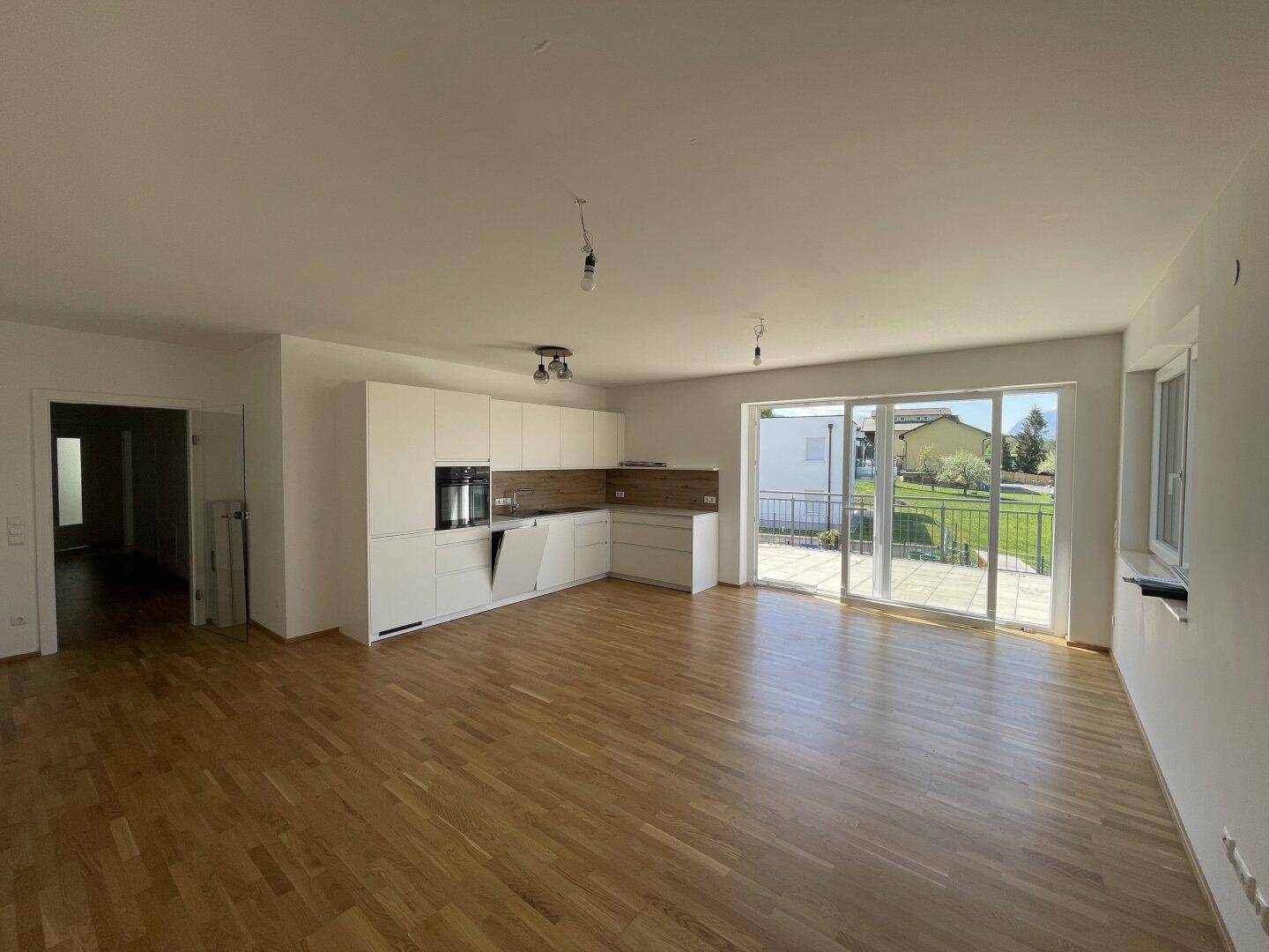 Heller offener Wohnbereich mit integrierter Küche, Parkettboden und Zugang zur Terrasse.