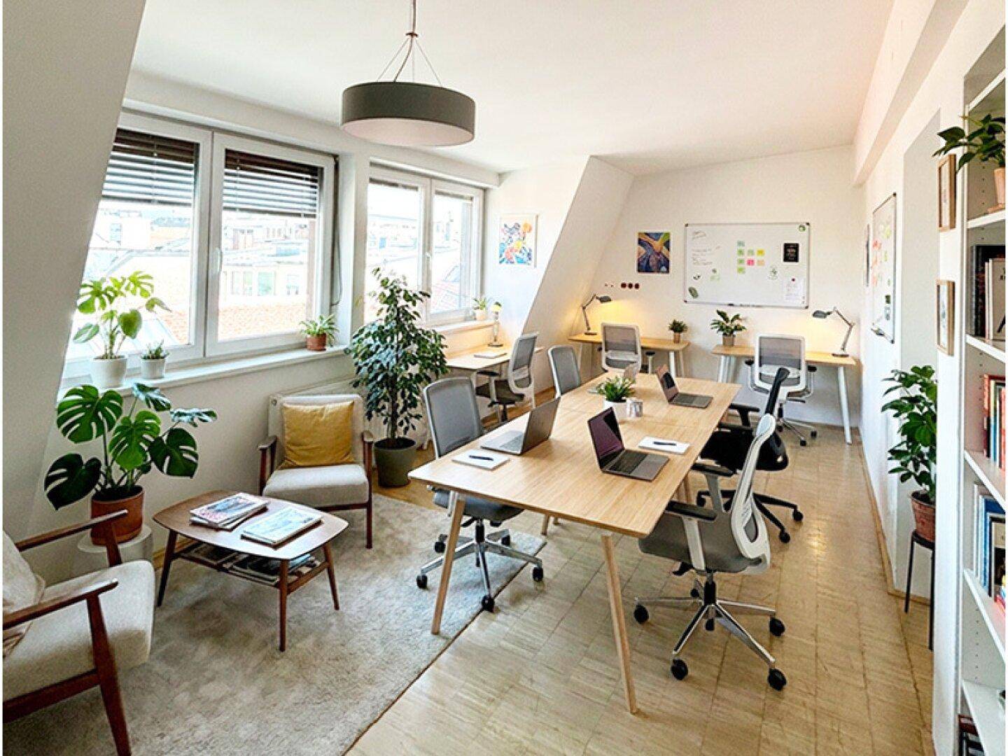 Helles Büro mit mehreren Arbeitsplätzen, Holzböden und vielen Pflanzen, unter einem Dachschrägenfenster.