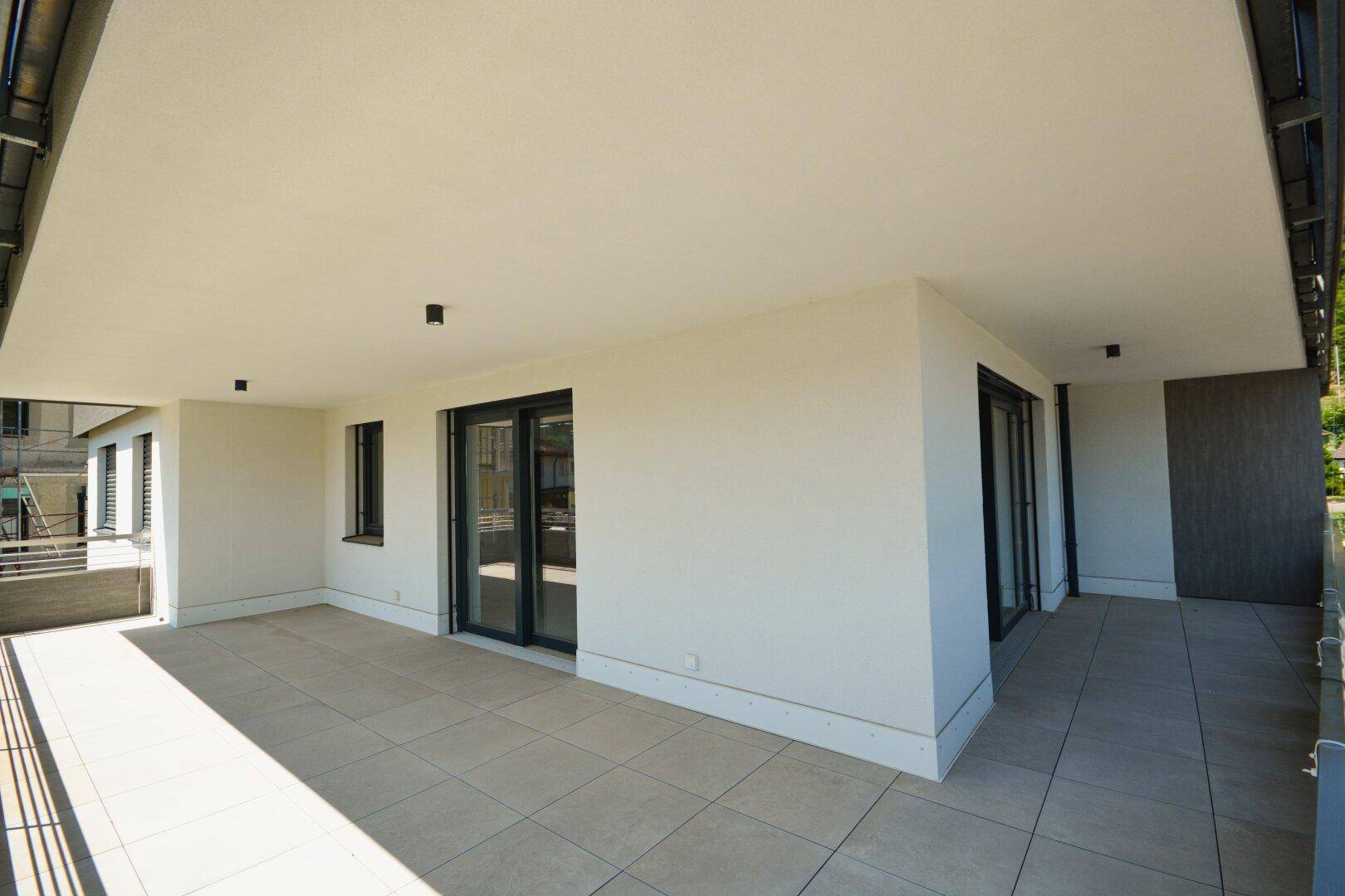 Geräumige, überdachte Terrasse mit Fliesenboden und Zugang zu mehreren Innenräumen.