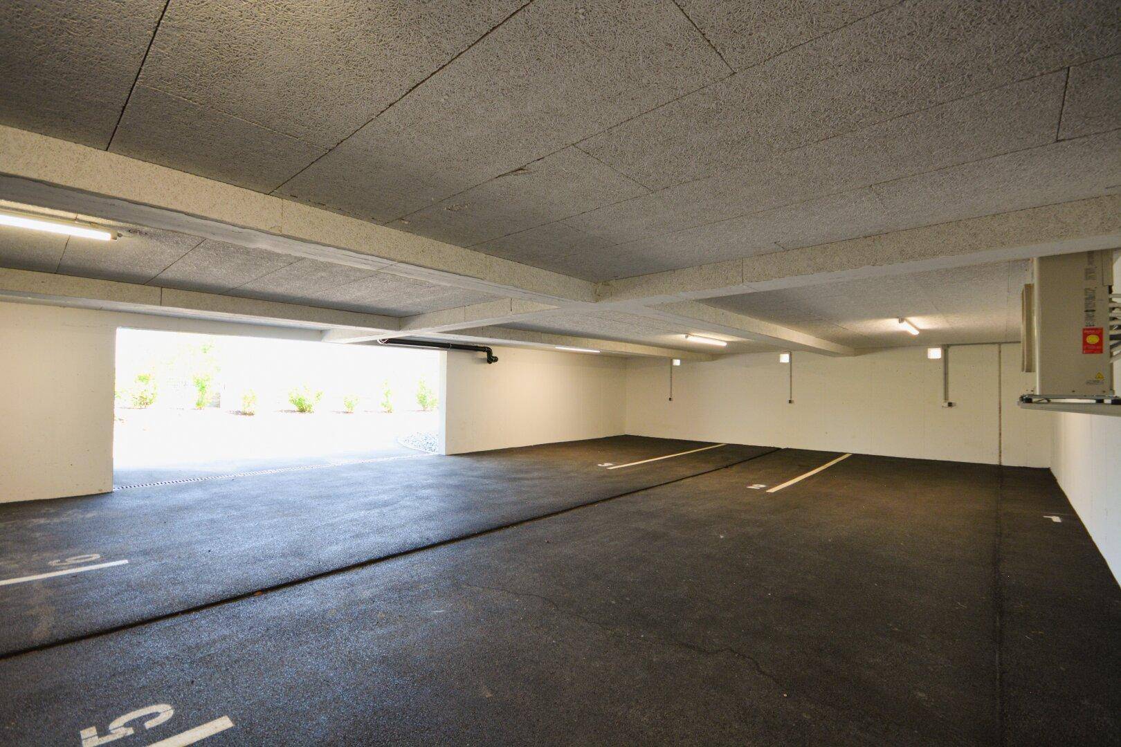 Geräumige und helle Tiefgarage mit mehreren markierten Stellplätzen für Fahrzeuge.