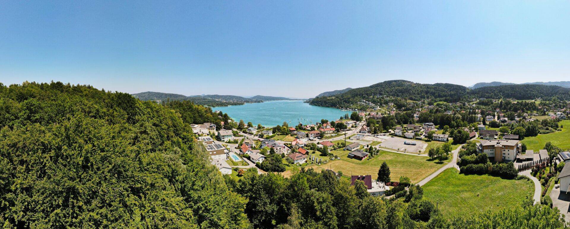 Panoramablick auf eine malerische Stadt am See, umgeben von bewaldeten Hügeln und Bergen.