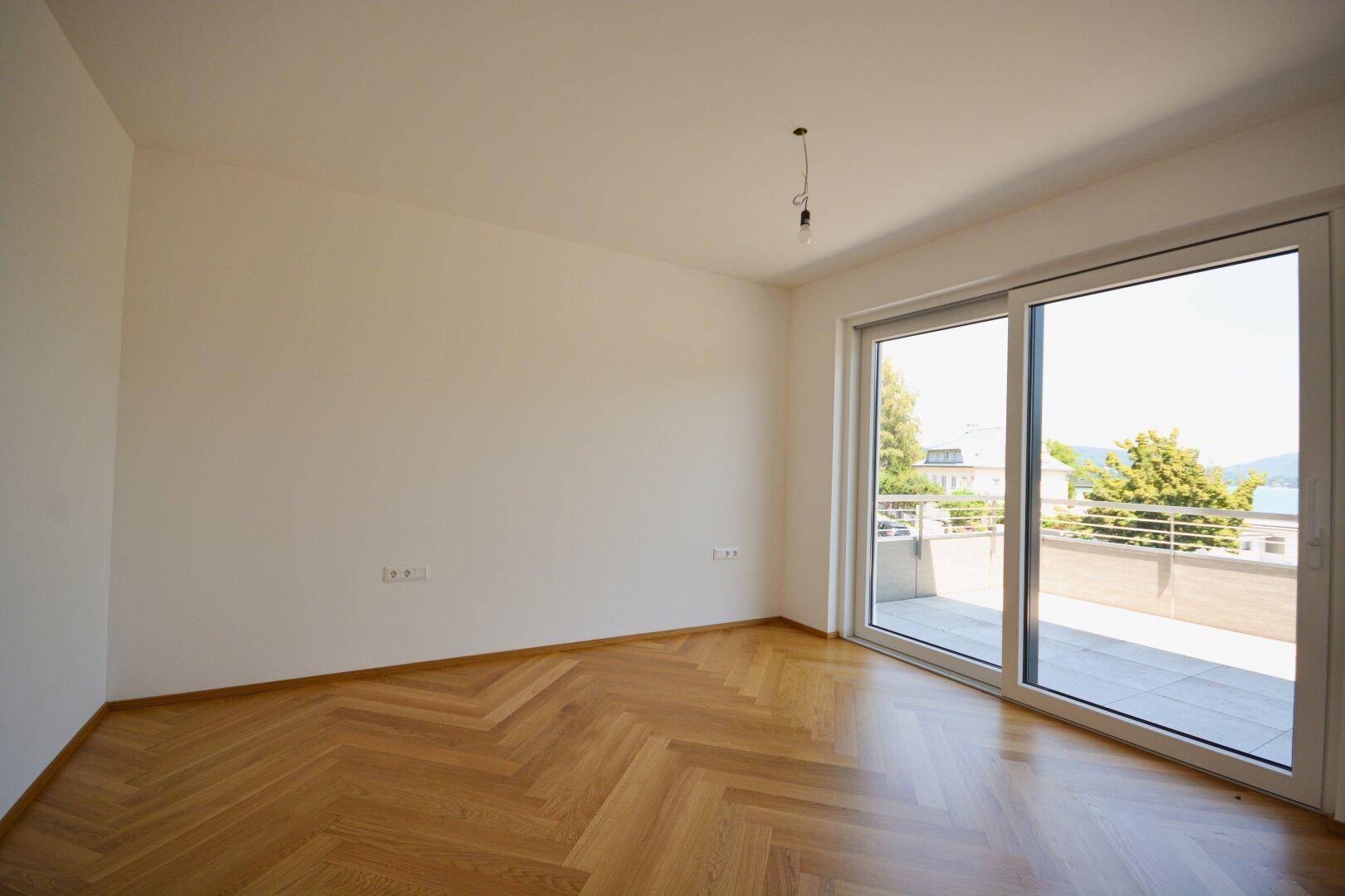 Helles Schlafzimmer mit Fischgrätparkett und großem Fenster, das Zugang zu einer sonnigen Terrasse bietet.