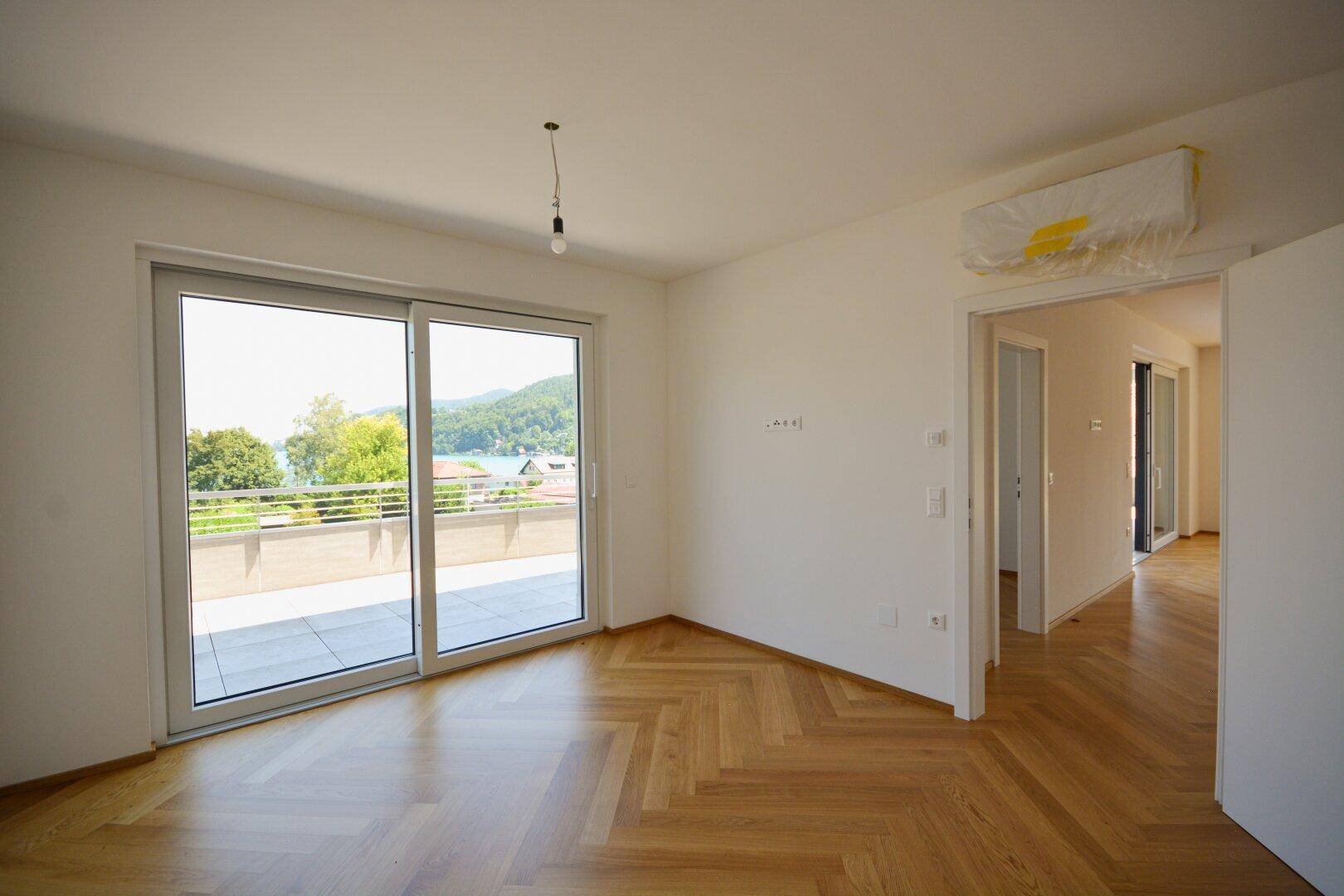 Helles Zimmer mit Fischgrätparkett, großen Schiebetüren und direktem Zugang zur Terrasse mit Seeblick.