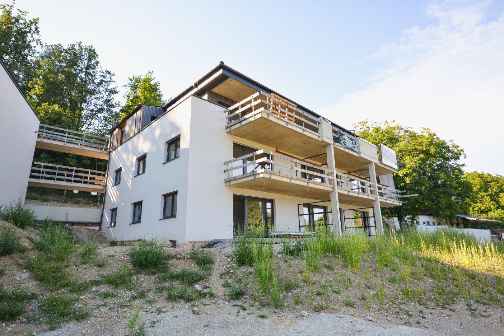 Modernes Mehrfamilienhaus im Bau mit mehreren Balkonen und Blick ins Grüne.