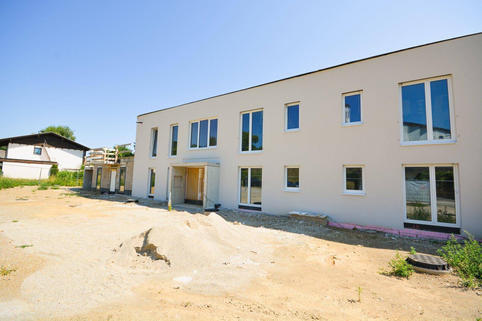 Fassade des Neubaus mit großen Fenstern und unfertigem Eingangsbereich auf dem Baugelände.
