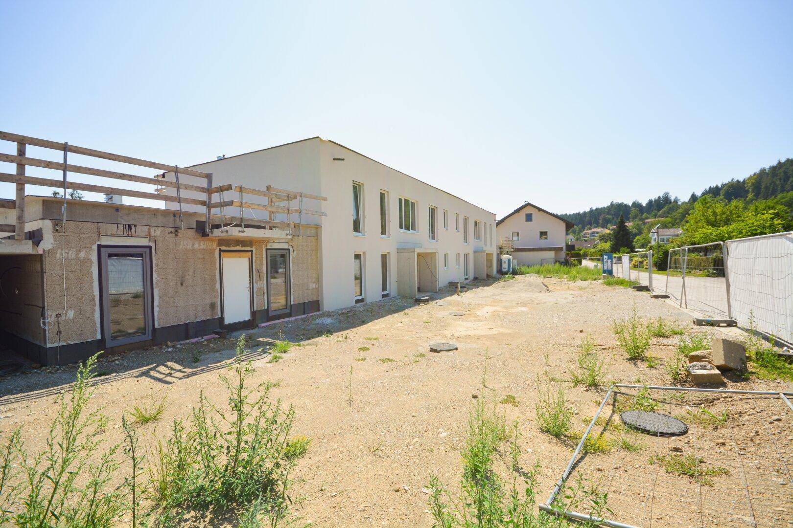 Ansicht eines im Bau befindlichen Gebäudes mit weißer Fassade und umliegendem Baustellenbereich.