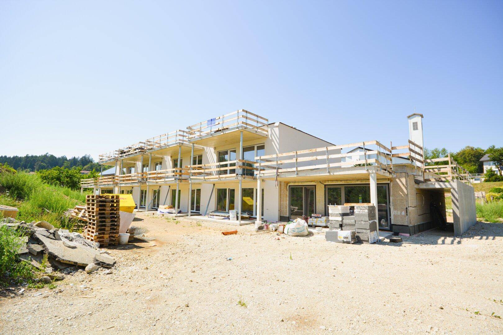 Rückansicht des Neubaus mit mehreren Balkonen und Baustellenmaterialien im Vordergrund.