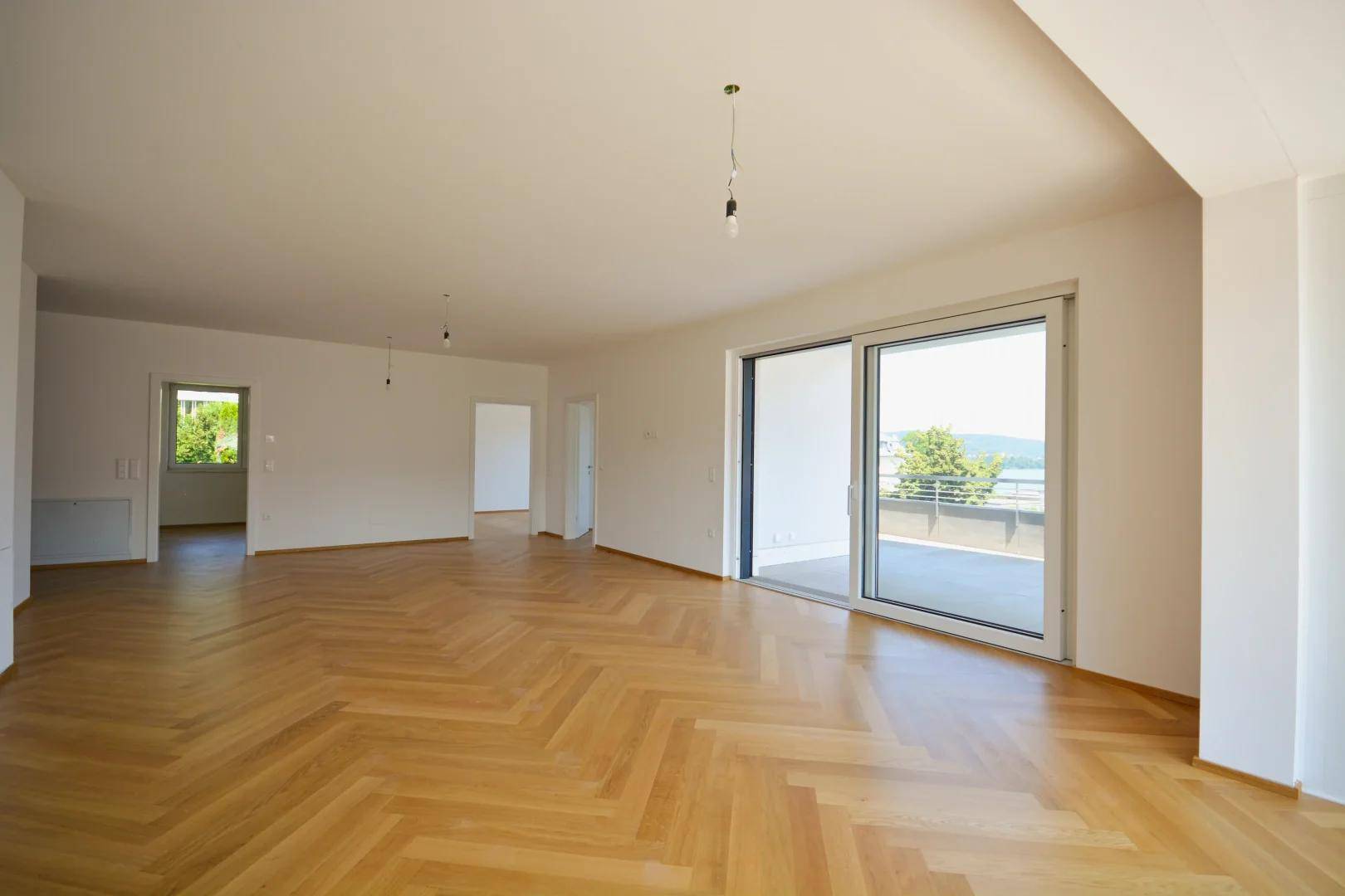 Heller, geräumiger Wohnbereich mit Fischgrätparkett und großem Schiebefenster zum Balkon mit Seeblick.