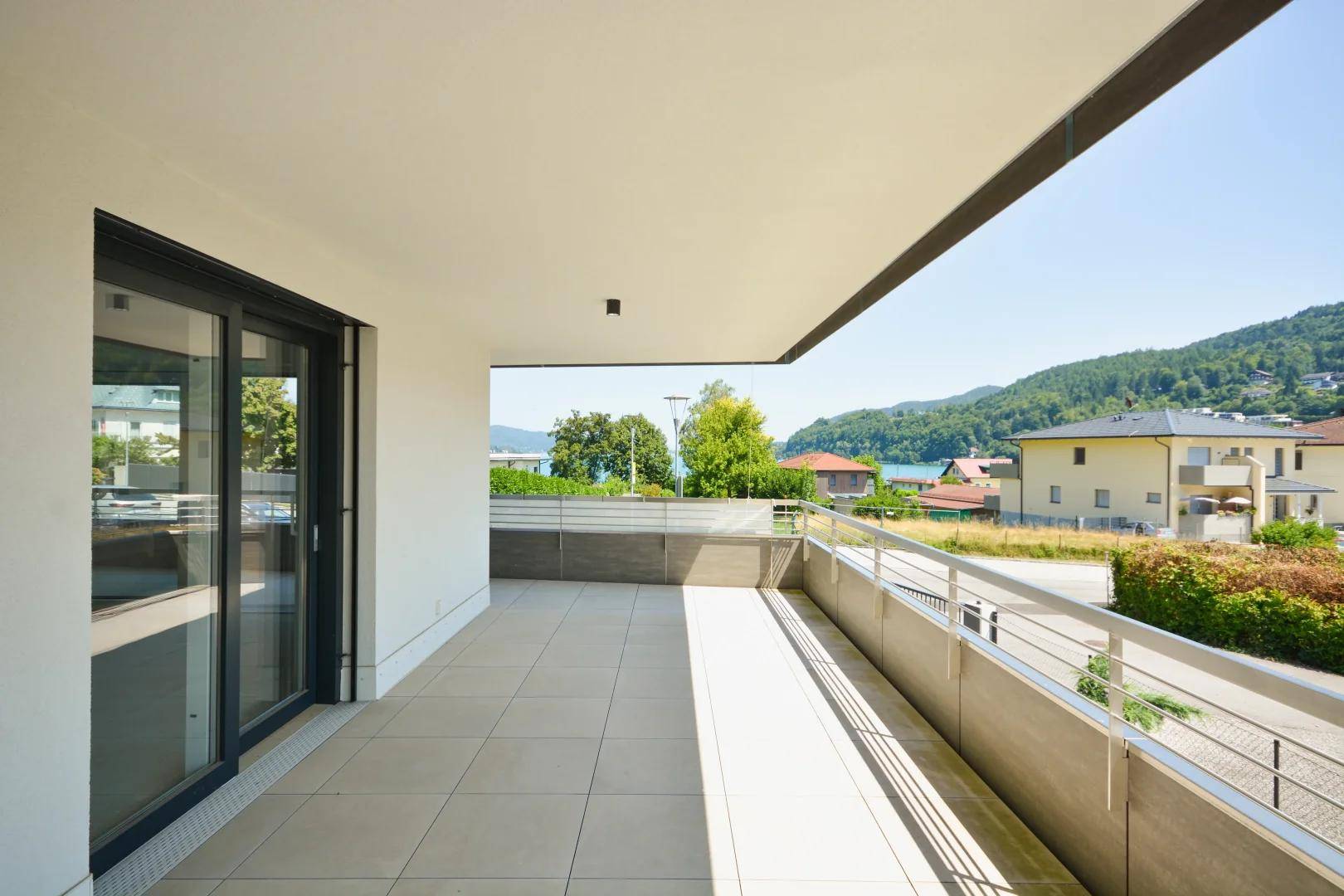 Großer Balkon mit Fliesenboden und Metallgeländer bietet einen weiten Blick auf den See und die umliegende Landschaft.