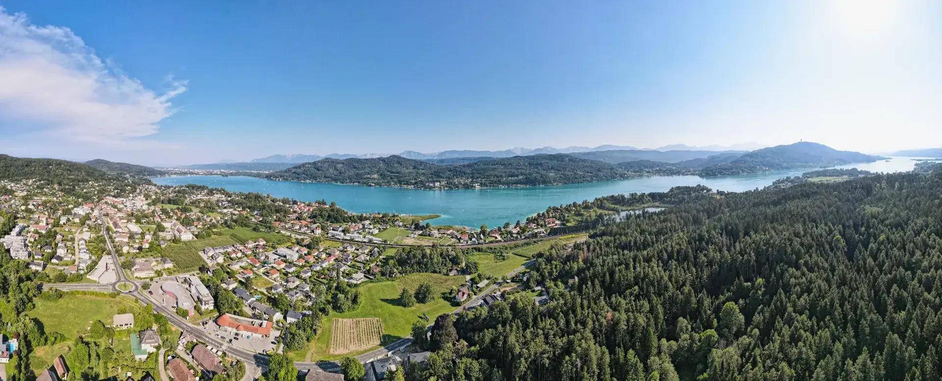 Panoramablick über eine Stadt am See, umgeben von Wäldern und Bergen unter blauem Himmel.