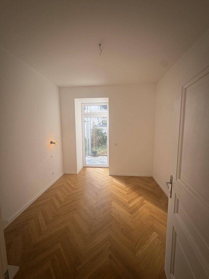 Helles Schlafzimmer mit Fischgrätparkett und direktem Zugang zu einem Außenbereich.