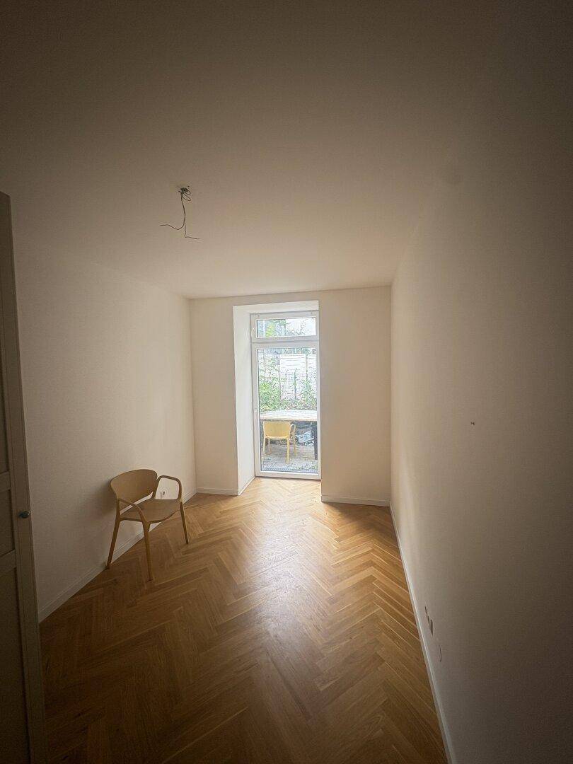 Freundliches Zimmer mit Fischgrätparkett und großem Fenster, das viel Tageslicht hereinlässt.