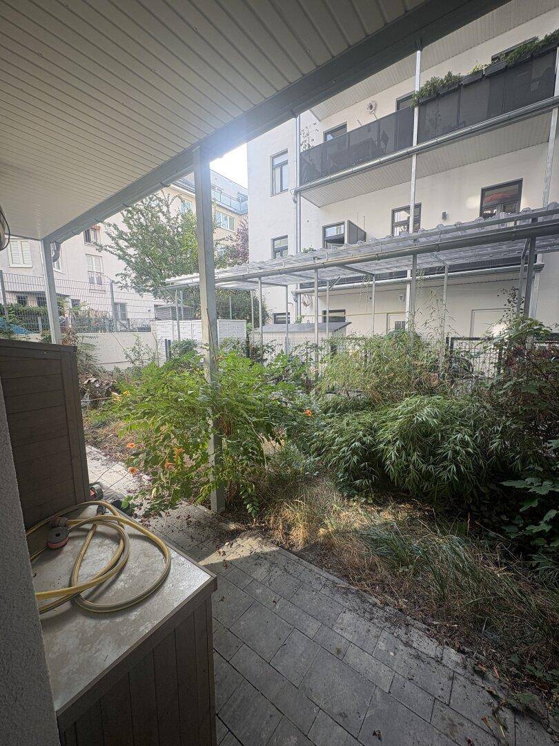 Gartenbereich mit Terrasse und Blick auf die Rückseite des Gebäudes mit Balkonen.