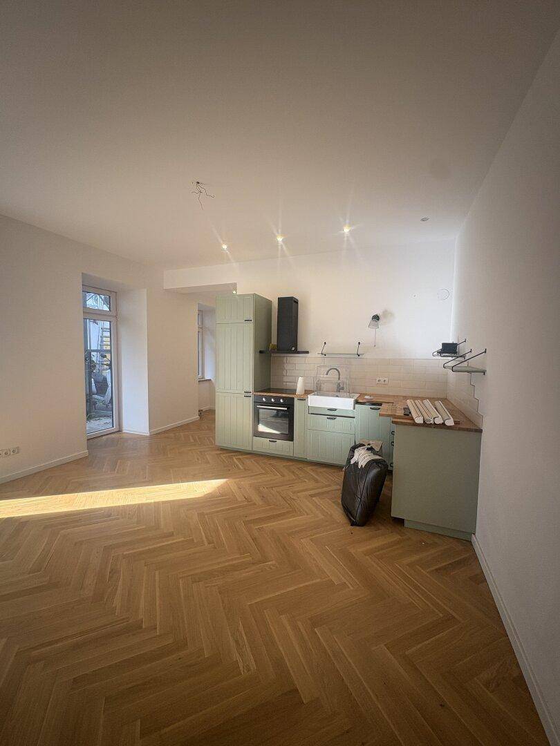 Geräumiger offener Wohnbereich mit moderner Einbauküche und hellem Fischgrätparkettboden.