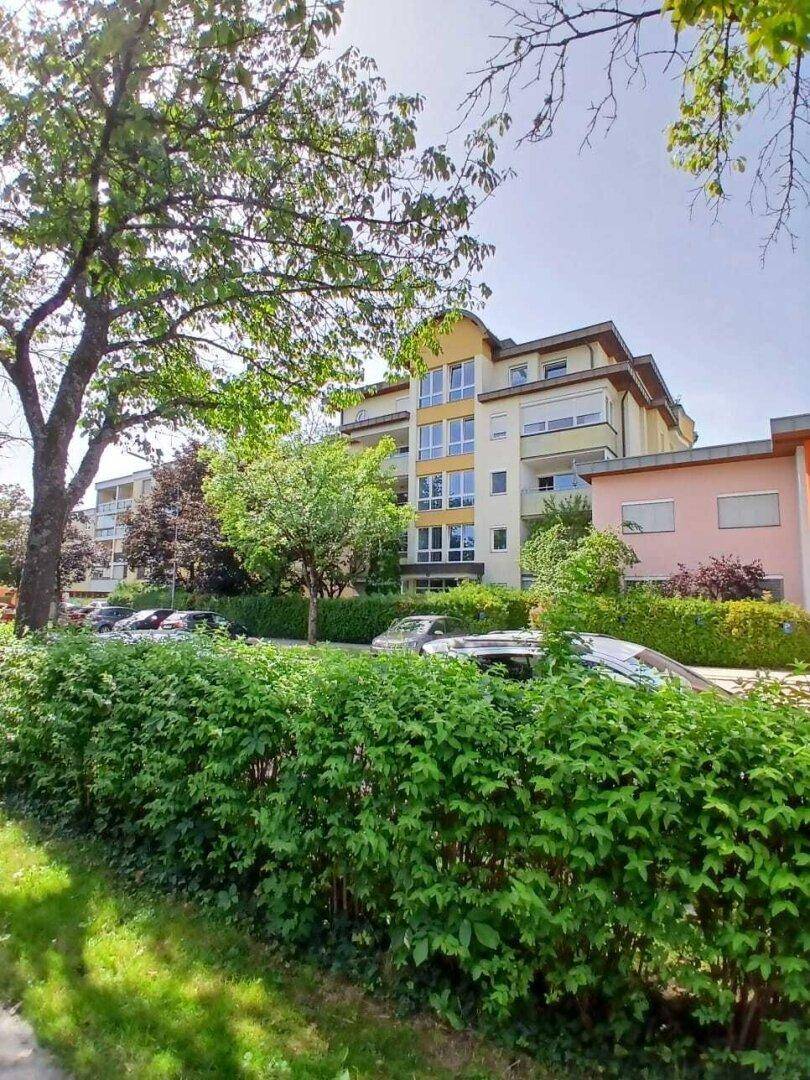 Mehrfamilienhaus mit moderner Architektur, umgeben von Bäumen und einer gepflegten Hecke.