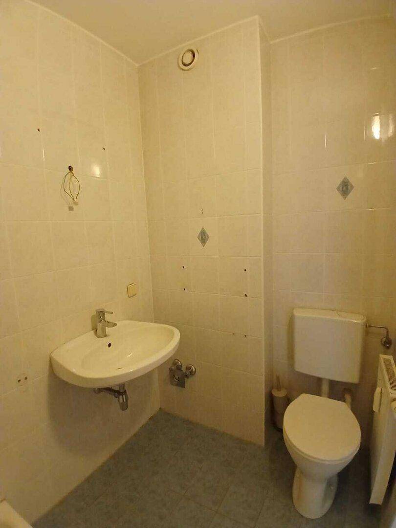 Funktionales Badezimmer mit beigefarbenen Wandfliesen, Waschbecken und WC, in gutem Zustand.