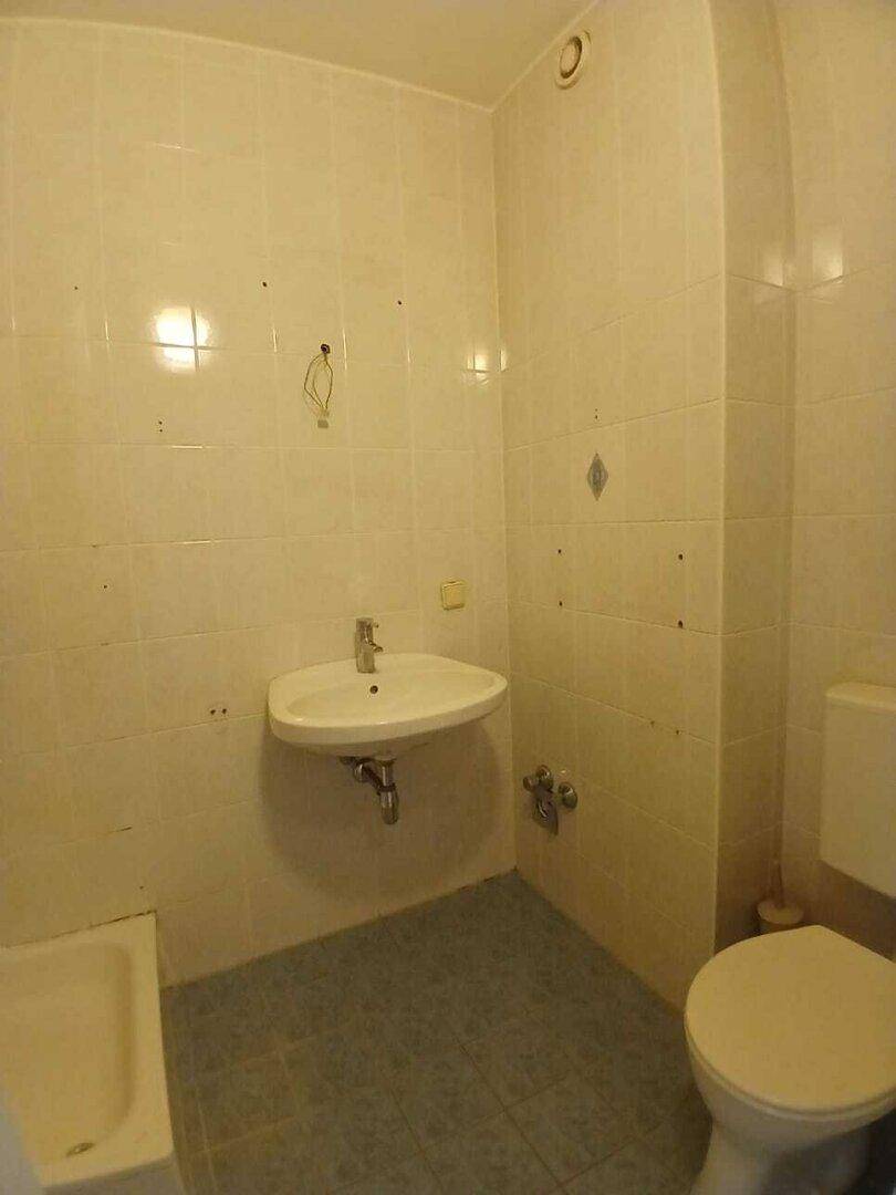 Kleines Badezimmer mit hellen Fliesen, Waschbecken und Toilette, ausgestattet mit einer Badewanne.