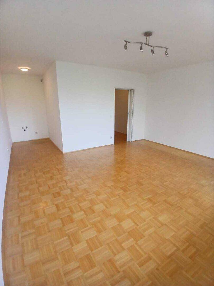 Geräumiges, leeres Wohnzimmer mit hellem Parkettboden und weiß gestrichenen Wänden, bereit zur Einrichtung.