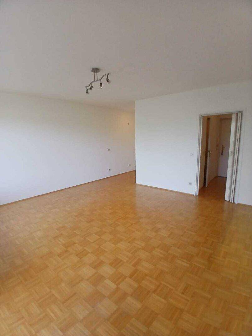 Weitläufiges Wohnzimmer mit klassischem Parkettboden und neutralen Wänden, bietet viel Platz für Möbel.