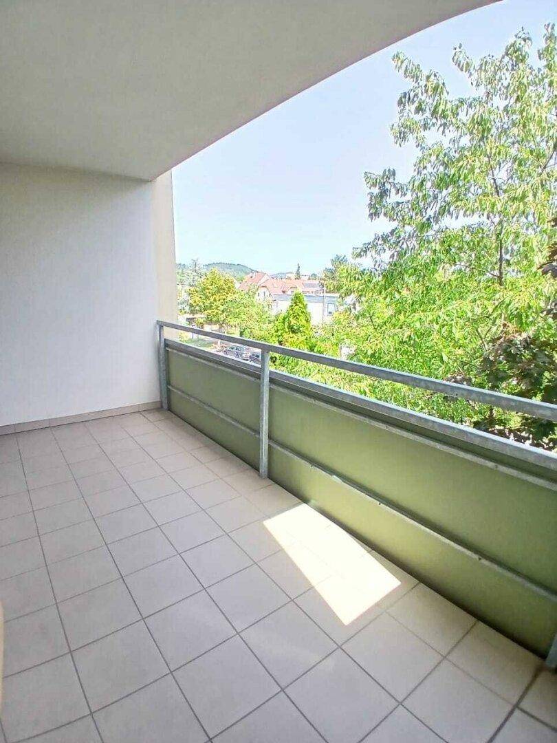Heller Balkon mit Fliesenboden und grüner Brüstung, bietet einen angenehmen Blick ins Grüne.