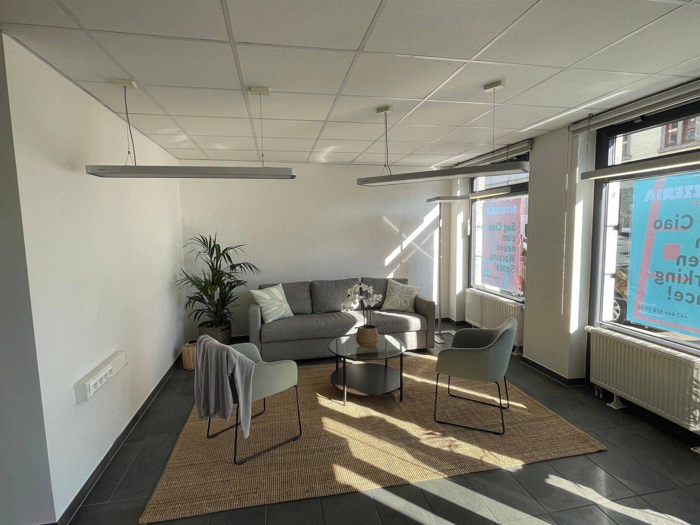 Heller Lounge-Bereich mit modernen Möbeln, großen Fenstern und Fliesenboden, ideal für Wartezonen.