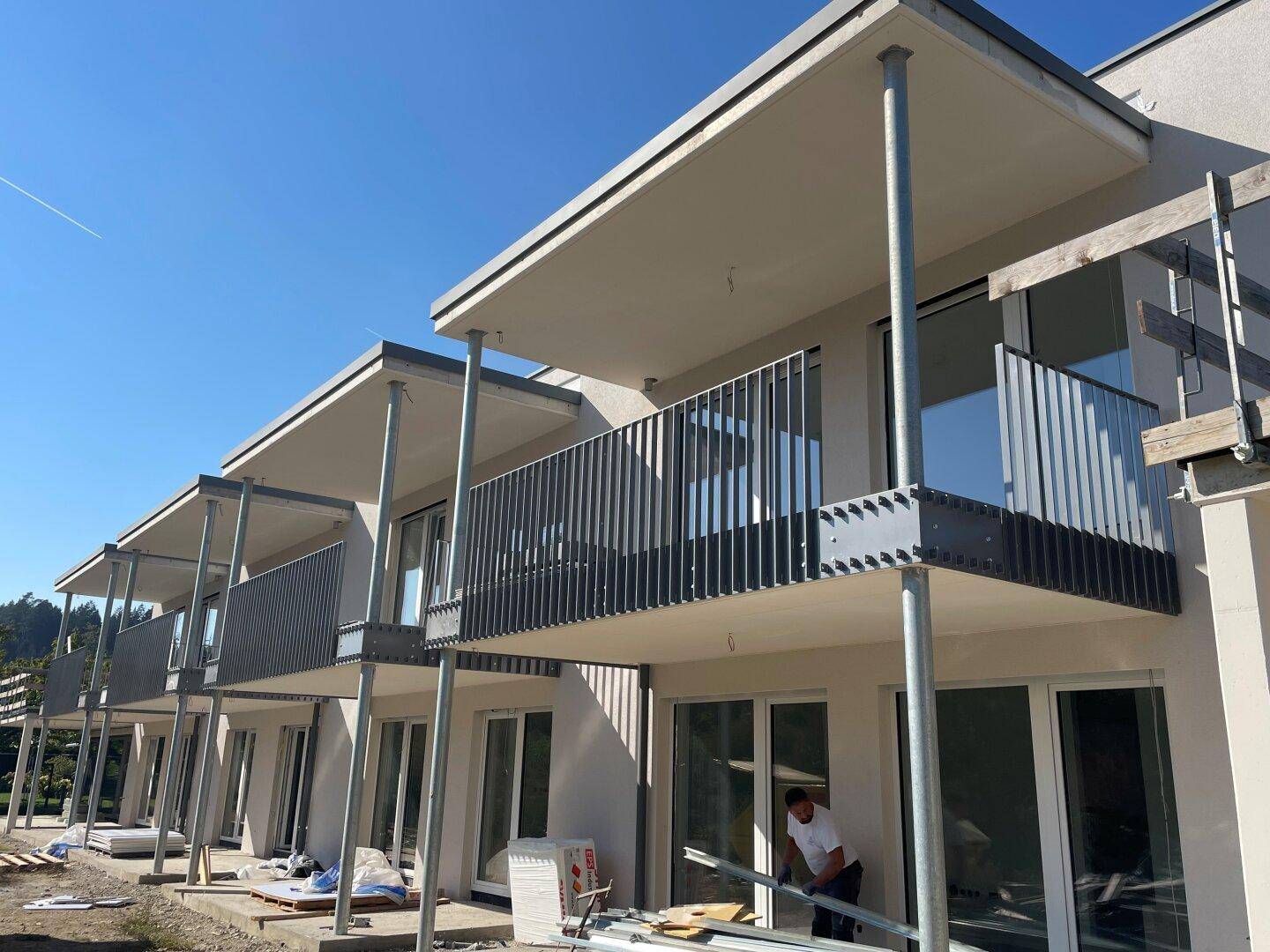 Neubau mit modernen Balkonen und großen Fenstern während der Bauphase unter blauem Himmel.