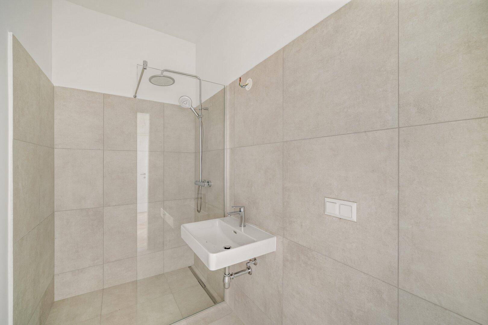 Modernes Badezimmer mit begehbarer Dusche, Wandwaschbecken und hellen Fliesen.
