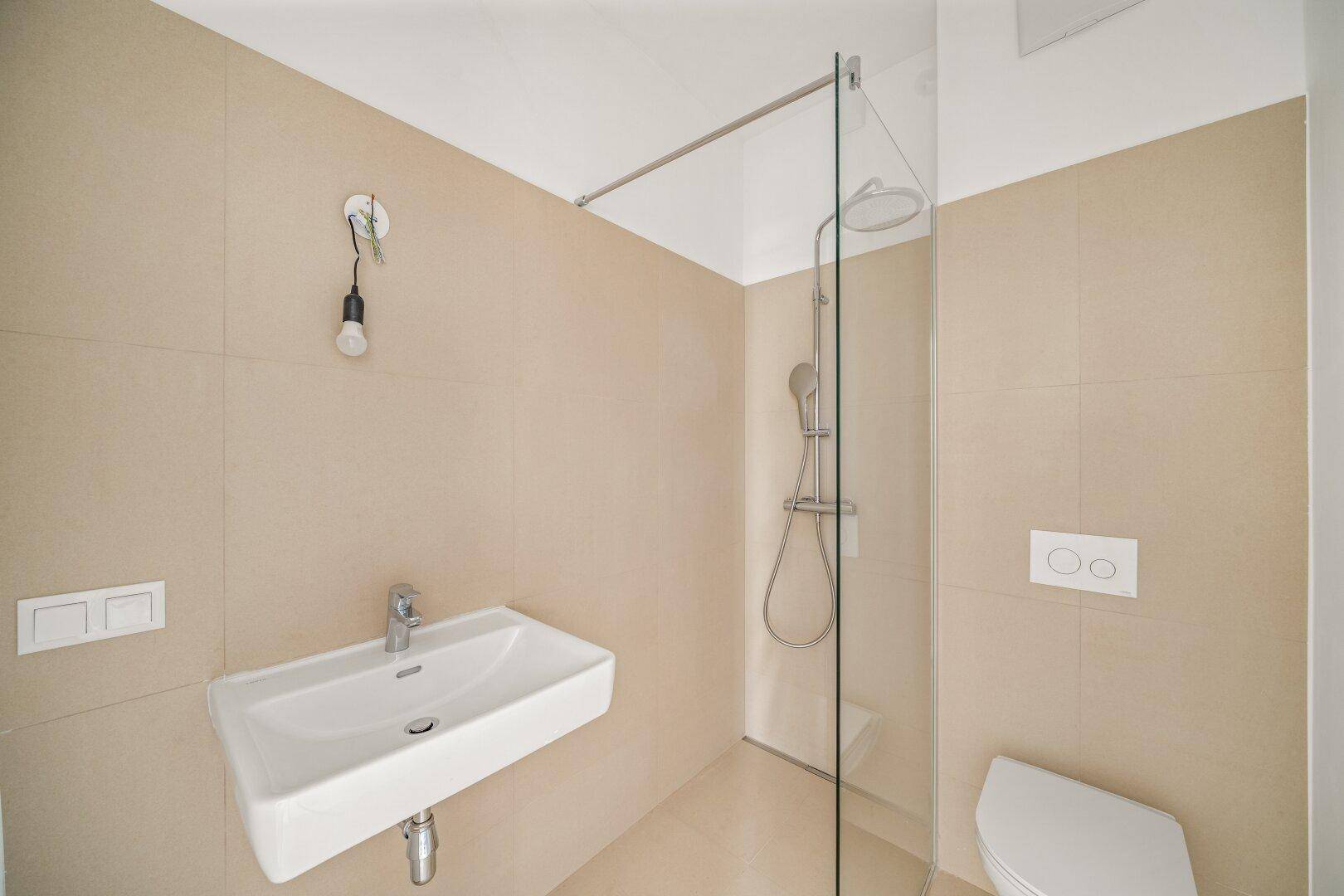 Modernes Badezimmer mit beigefarbenen Fliesen, ebenerdiger Dusche und wandhängendem WC.