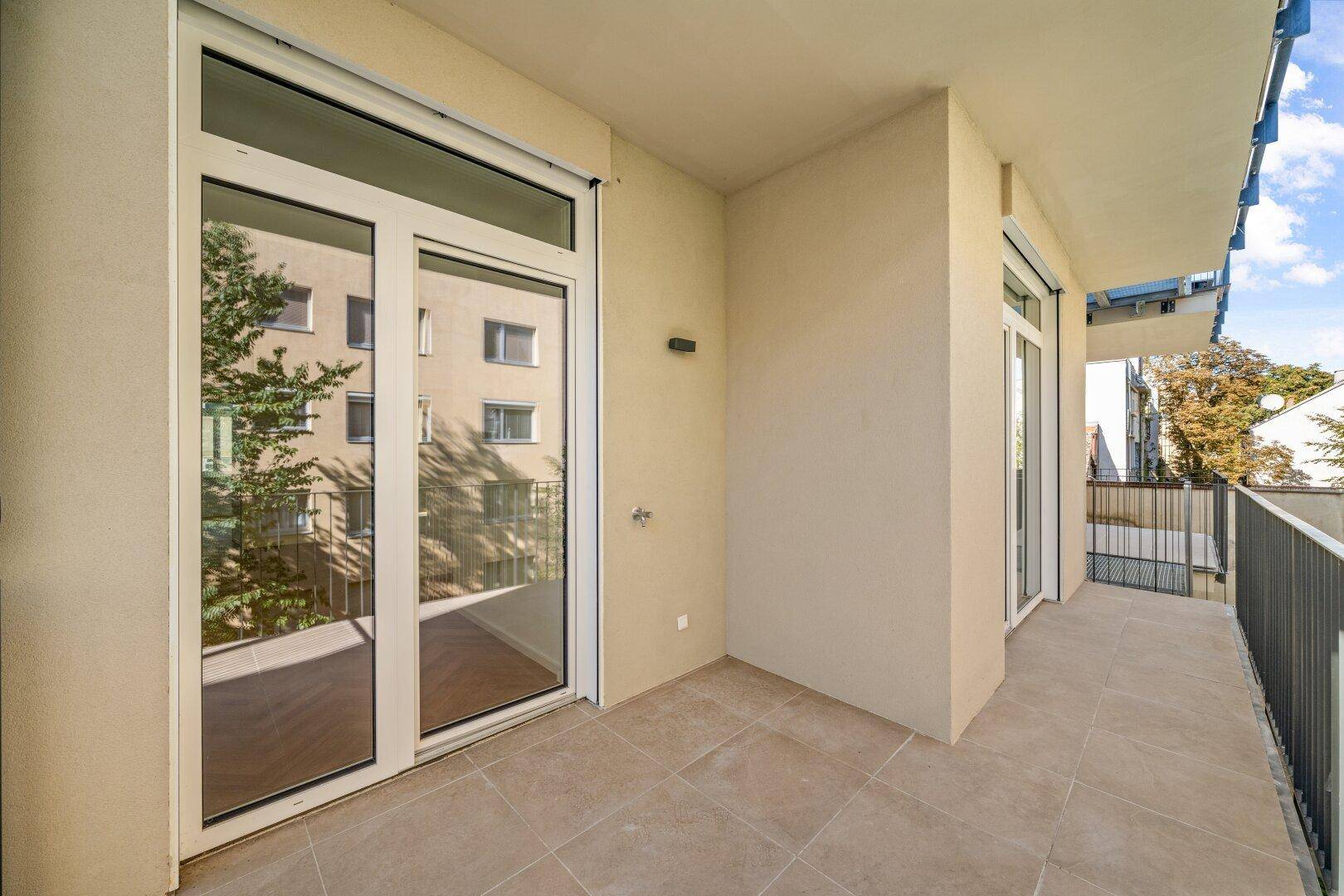Geräumiger Balkon mit Fliesenboden und Blick auf die umliegenden Gebäude und Bäume.