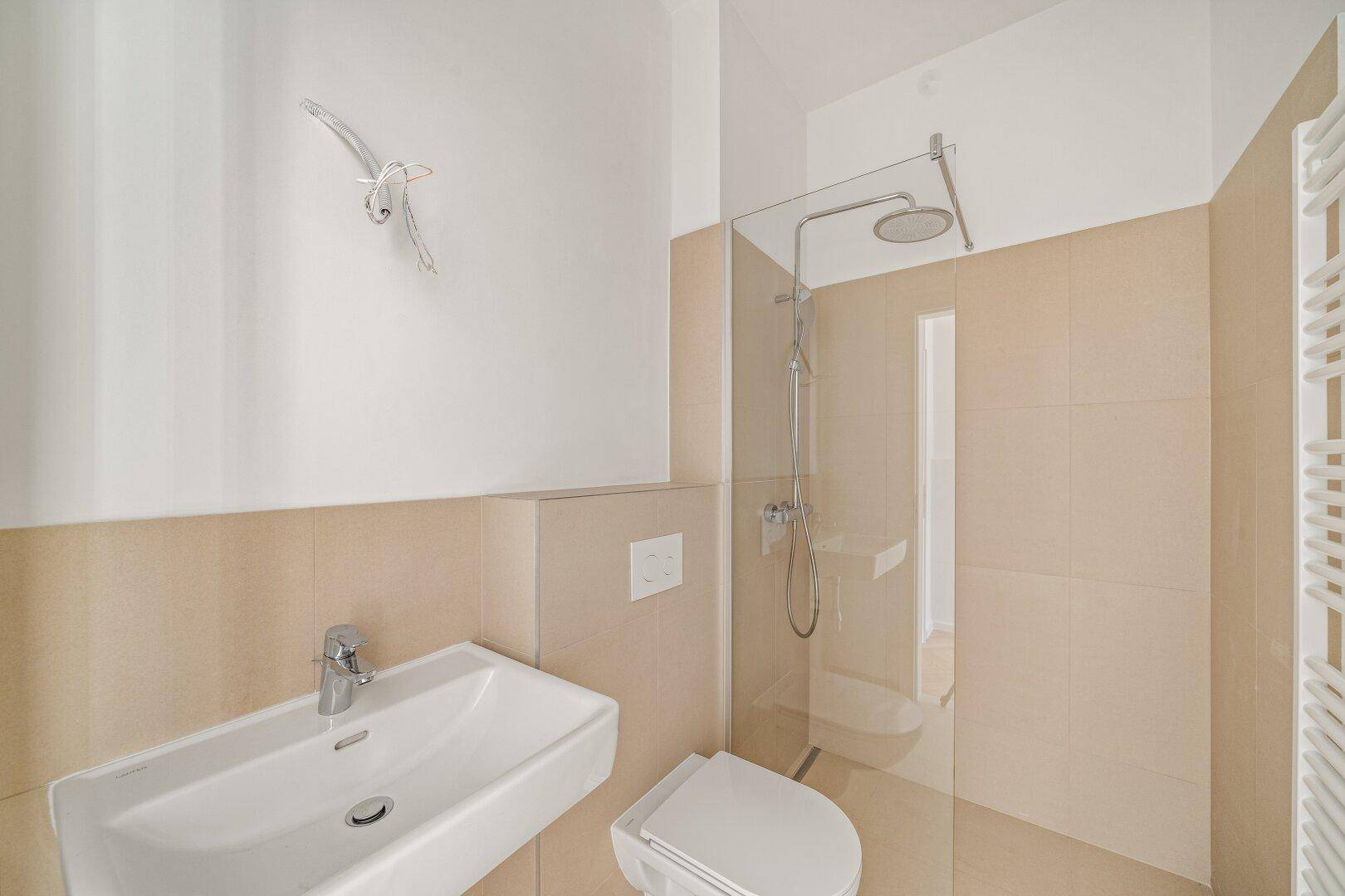 Zeitgemäßes Badezimmer mit beigefarbenen Fliesen, Regendusche und beheiztem Handtuchhalter.