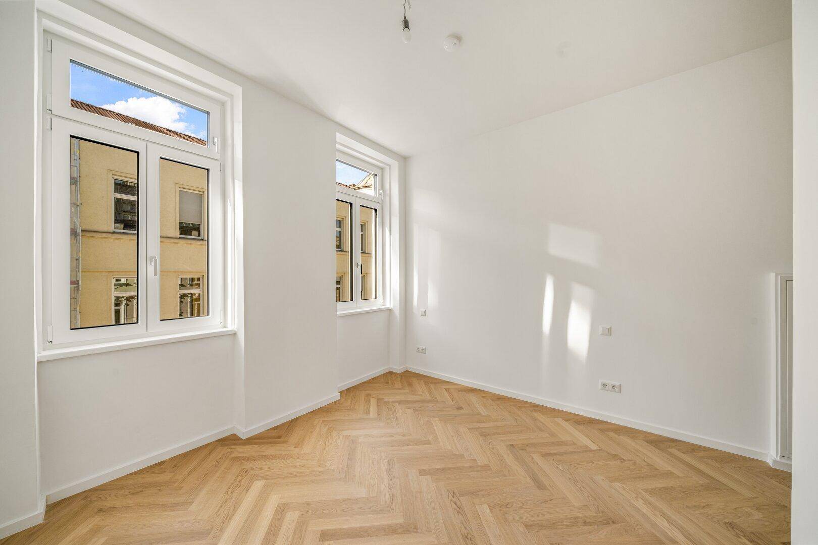 Helles Schlafzimmer mit zwei großen Fenstern und Fischgrätparkett, bietet viel Tageslicht.
