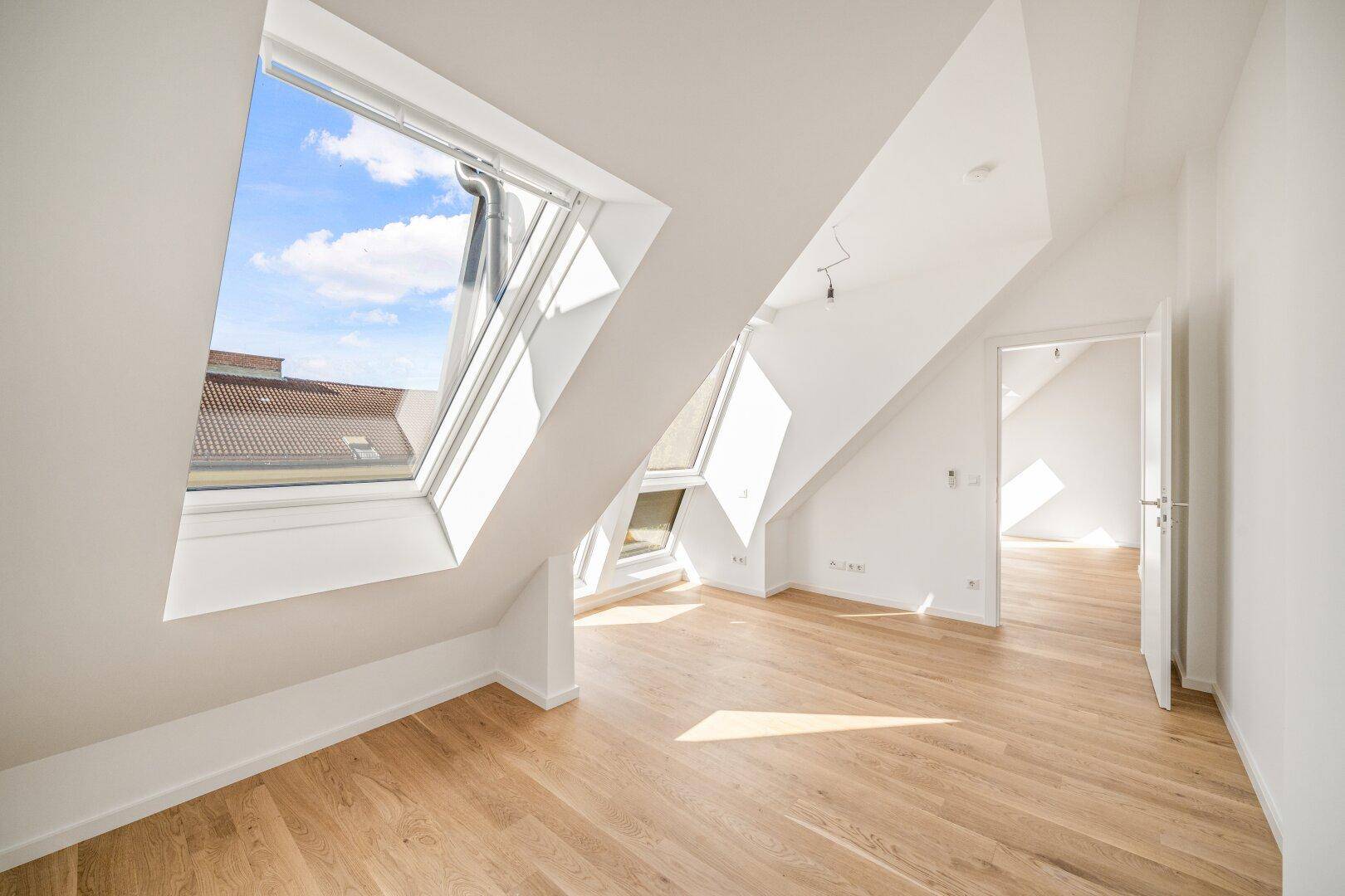 Lichtdurchflutetes Dachgeschosszimmer mit großen Dachfenstern und hellem Holzboden, ideal für Wohnzwecke.