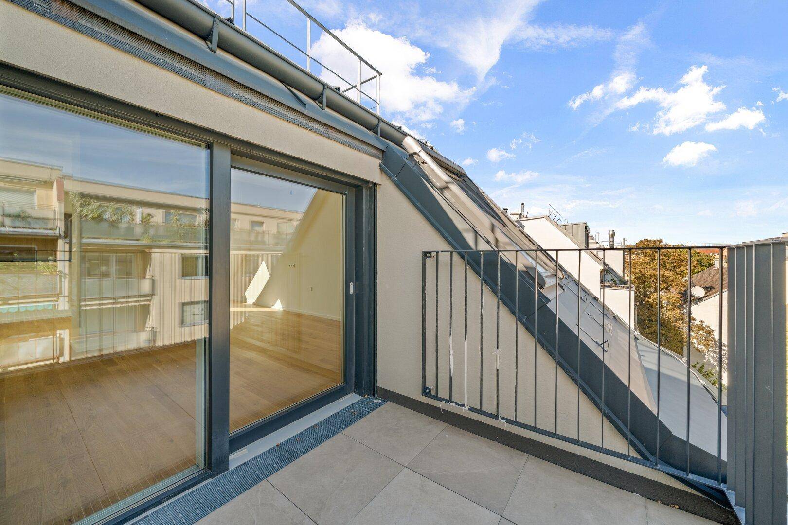 Dachterrasse mit Fliesenboden und Blick auf die umliegenden Gebäude, zugänglich durch eine Glasschiebetür.