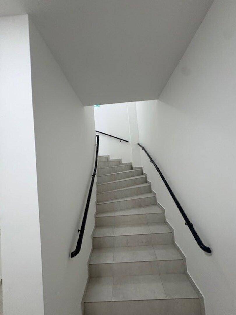 Helles Treppenhaus mit Fliesenstufen und schwarzem Handlauf in einem Mehrfamilienhaus.