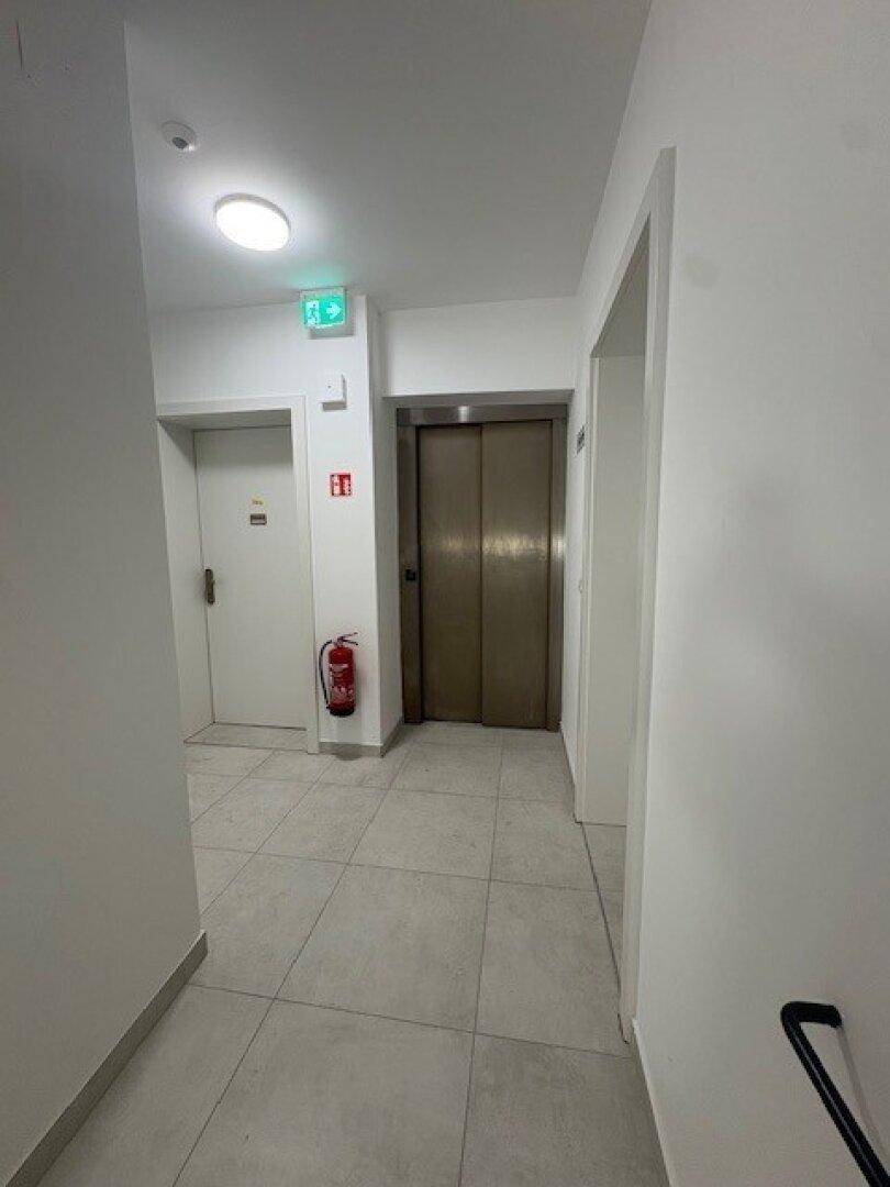 Moderner Flur mit Fliesenboden und Zugang zu einem Aufzug in einem Wohngebäude.